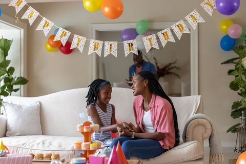 Mother and daughter celebrating birthday at home with colorful balloons and cupcakes