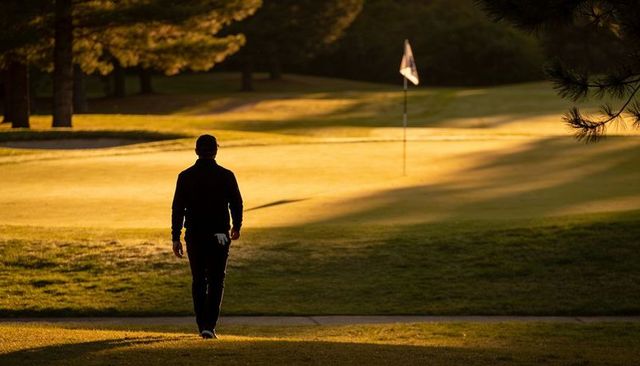 Solitary golfer walking toward flagstick during golden hour on quiet fairway
