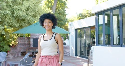 Smiling african american woman relaxing on sunny backyard patio in casual summer outfit