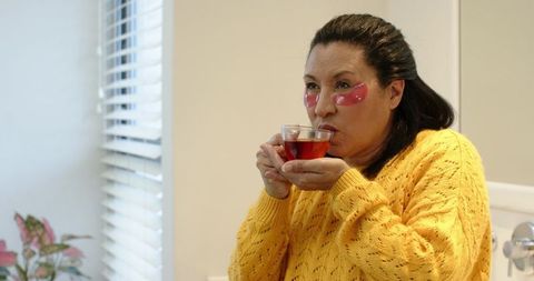 Woman in bathroom wearing eye patches and cozy yellow sweater