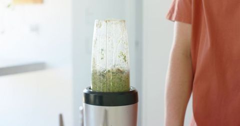 Compact personal blender blending green smoothie on kitchen counter with casual rust tee