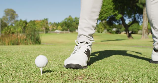 Photo depicts golfer preparing for a tee shot on a sunny day. Focus on the golfer’s foot and golf ball placed on the tee. Suitable for use in sports magazines, golf tutorials, athletic footwear ads, or articles about recreational activities.