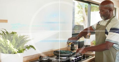 Senior man pouring olive oil into nonstick pan on modern gas stove, bright kitchen
