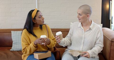 Sharing coffee and conversation between diverse female friends on cozy cafe sofa