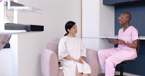 Hispanic Woman in Gown Consulting with African American Mammography Tech in Pink Scrubs
