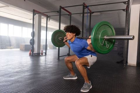 African american man performing barbell back squat in functional gym strength training