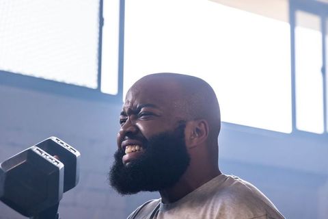 African american man lifting hex dumbbell, straining with determination in industrial gym