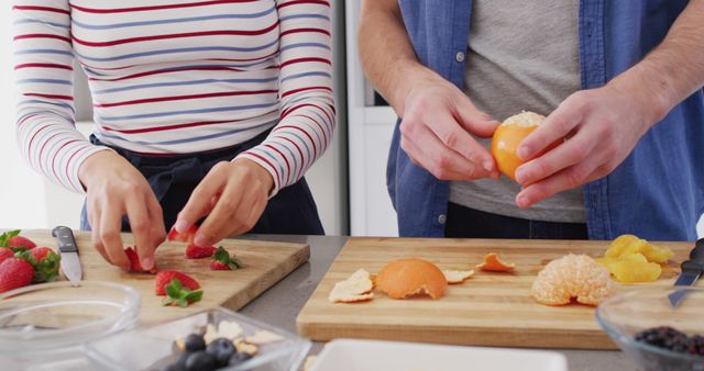 Capturing moment of people working together, preparing fresh fruits in a modern kitchen. Ideal for use in food blogs, healthy lifestyle promotions, cooking tutorials, and advertisements promoting healthy eating habits. Emphasizes teamwork and the importance of fresh eating.