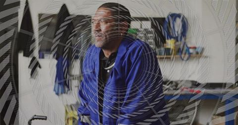 Mechanic leaning on workbench wearing blue jacket inspecting tools in industrial garage