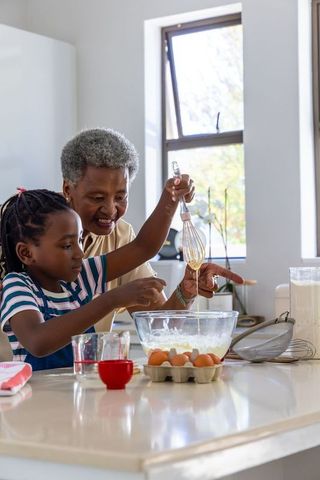 African american grandmother teaching granddaughter whisking batter and baking together
