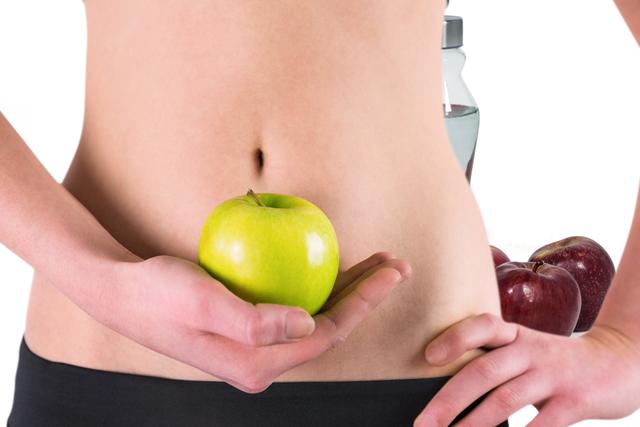 Depicting health and wellness through the midsection of a woman holding a green apple, this image is ideal for promoting fitness, healthy diets, nutrition, and lifestyle blogs. It is suitable for use on websites, social media campaigns, and marketing materials related to health, wellness, and dietary plans.
