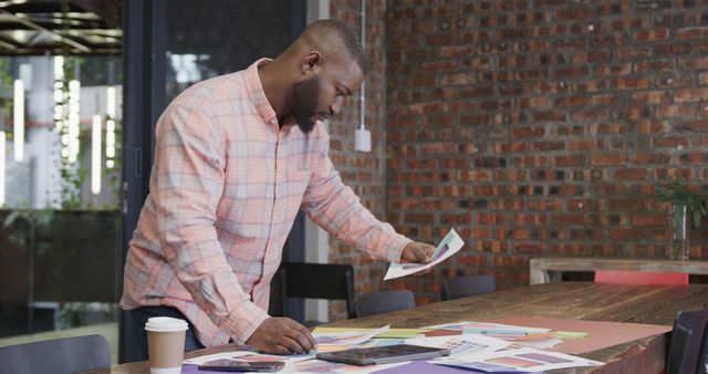 African american male designer holding pictures and using tablet at office. Casual business, communication, design and office, unaltered.