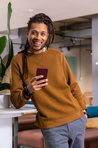 Laughing African American man leaning on bar with phone wearing brown sweater in coworking space