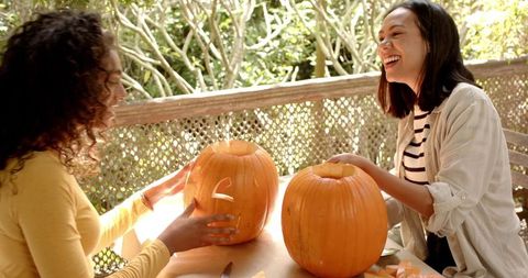 Multiracial Friends Carving Pumpkins for Halloween on Porch