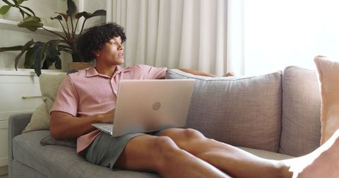 Man Relaxing on Sofa with Laptop, Sunlit Modern Living Room