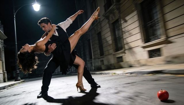 Couple dancing tango dip under streetlamp at night with dramatic lift and red apple