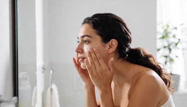 Applying moisturizer at bathroom mirror morning skincare routine sunlit minimal self-care