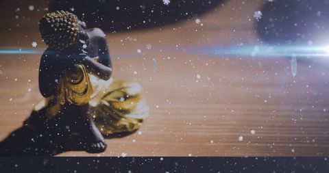 Meditative Buddha Statue with Snowflakes and Lens Flare on Wooden Table