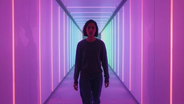 Woman Walking Through Neon LED Tunnel with Colorful Vertical Light Strips and Futuristic Vibe
