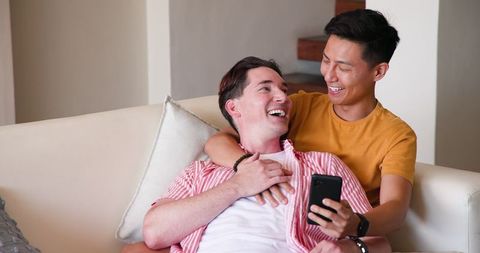 Affectionate Gay Couple Relaxed on Sofa Enjoying Smartphone Moment