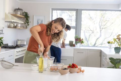 Diverse couple baking together in bright modern kitchen, woman whisking batter
