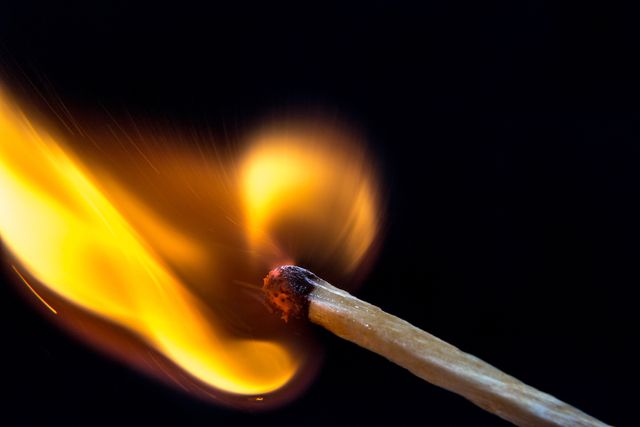 Close-up capture of a matchstick burning brightly against a black background. The image perfectly illustrates the ignition process and the dramatic lighting effects when fire is captured in a controlled macro shot. This picture can be used in fire safety presentations, educational materials, advertising for matches or fire-related products, and creative projects that require stunning visuals of combustion.