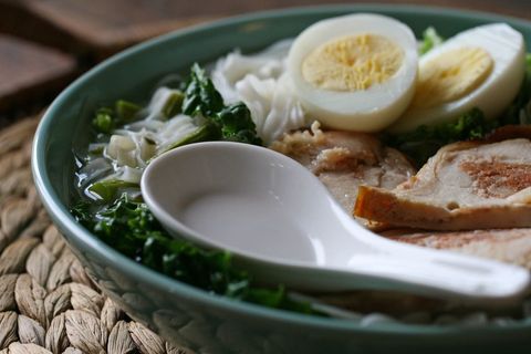 Steaming asian noodle soup with sliced chicken, boiled egg, rice noodles and greens