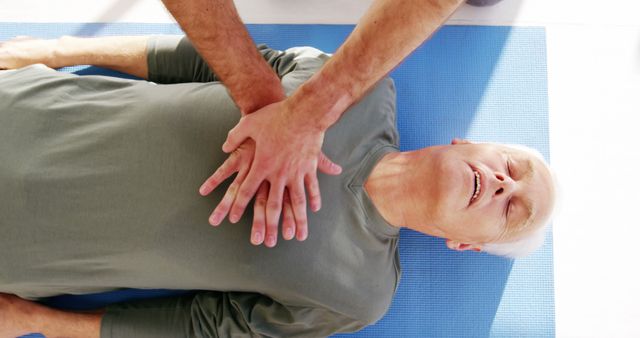 Person administering CPR to elderly man lying on blue mat, useful for emergency situations, medical training, CPR tutorials, first aid classes, lifesaving techniques demonstrations.