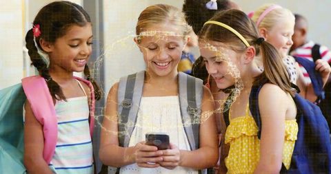 Elementary girls checking smartphone in school hallway smiling and sharing with backpacks
