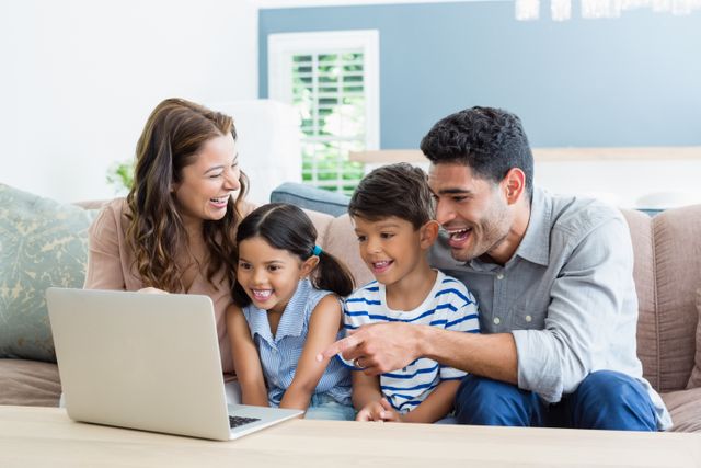 Parents and kids sitting in living room using laptop, bonding and enjoying time together. Ideal for content related to family life, modern technology use, parenting, home lifestyle, and digital communication.