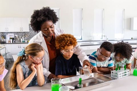 Diverse elementary students learning chemistry with teacher guiding hands-on experiment