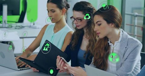 Three women collaborating on sustainable tech solutions reviewing devices and files