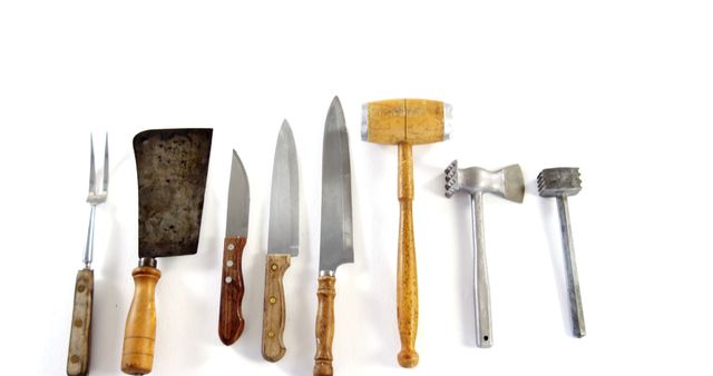 This image shows a collection of vintage butcher tools laid out on a white background. This collection includes various knives, a cleaver, a two-pronged carving fork, a wooden mallet, and meat tenderizers, all with wooden and metal handles. Perfect for use in historical kitchen settings, retro-themed design projects, food preparation articles, or vintage kitchen equipment retrospectives.