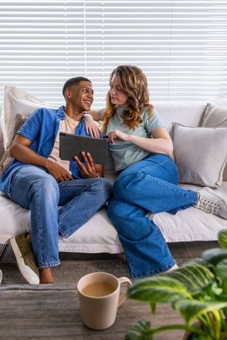 African american couple sharing tablet and coffee on sofa, relaxing at home