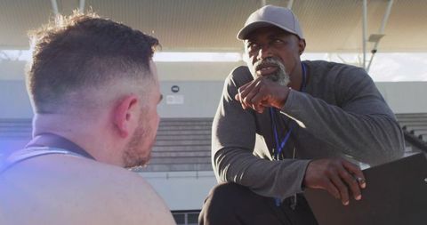 Kneeling coach motivating athlete on bleachers during outdoor stadium training session