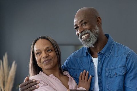 Smiling mature couple embracing at home in cozy denim and pink blouse, affectionate moment