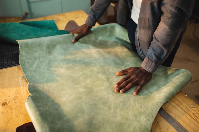 African American craftsman working with green leather at a workbench. Ideal for content related to handmade crafts, small businesses, artisans, and leatherworking. Useful for illustrating craftsmanship, creativity, and the process of creating handmade goods.