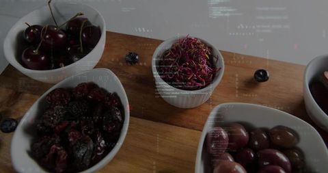 Ceramic bowls holding cherries olives and dried fruit on rustic wooden cutting board