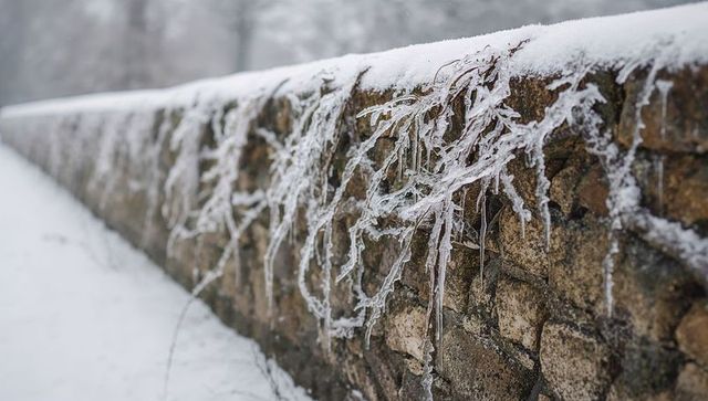Stone wall slanting through snowy park, snowcapped, iced grasses and hanging icicles