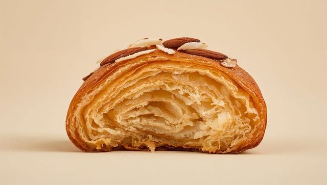 Buttery almond croissant half showing airy laminated layers flaky golden crust topped with almonds