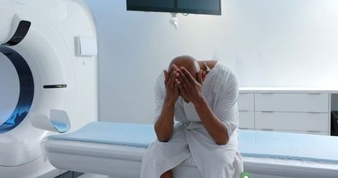 African american man covering face on hospital ct table expressing medical anxiety