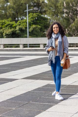 Young woman walking with smartphone and takeaway coffee across geometric urban plaza
