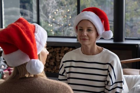 Middle-aged women wearing santa hats chatting on cozy living room sofa beside firewood