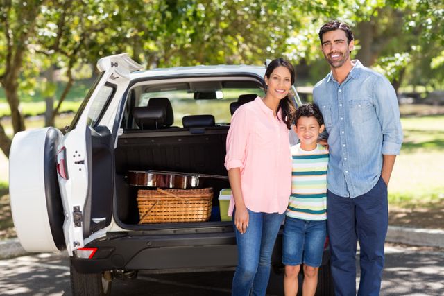 Family enjoying a picnic outing, standing next to their car with a picnic basket in the trunk. Ideal for use in advertisements for family cars, travel agencies, outdoor activities, and lifestyle blogs.