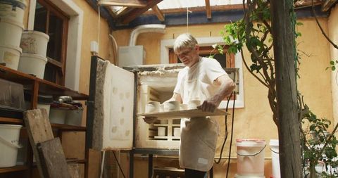 Senior Potter Unloading Ceramic Pieces from Kiln