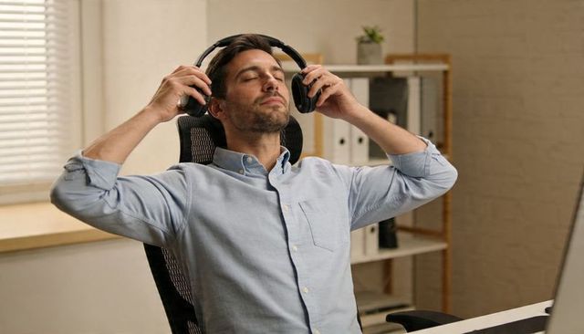 Relaxing professional man adjusting over-ear headphones at home office desk for focus