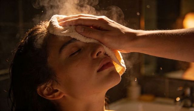 Woman receiving hot-towel facial in spa with warm steam and relaxing low-light ambience