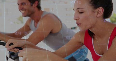 Woman cycling with digital metrics overlay during indoor spin class training with partner