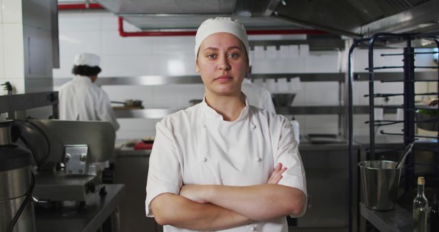 Portrait of caucasian female chef with arms crossed looking at camera. Working in a busy restaurant kitchen.