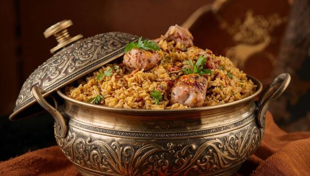 Ornate brass pot serving spiced chicken biryani with cilantro garnish and warm tones